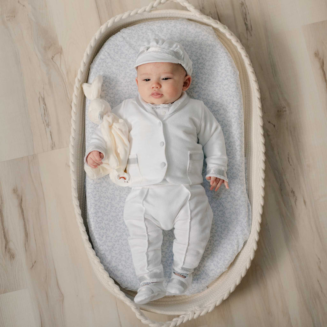 Newborn baby in the Henry 3-Piece Suit lying in a wicker bassinet with the Henry Silly Bunny Buddy. Perfect as a baptism gift from godparents.
