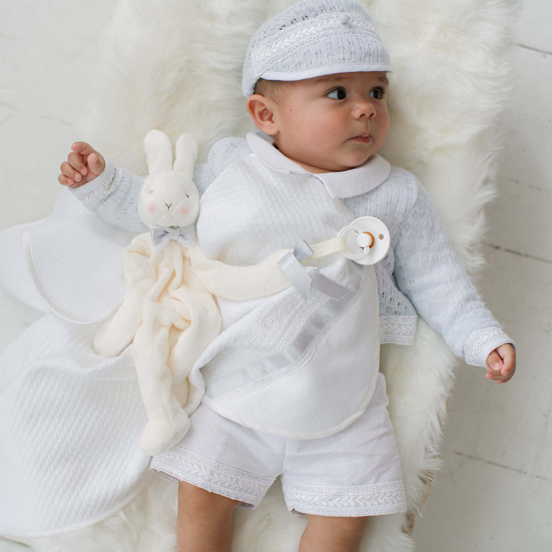Baby in a light blue outfit with a white plush bunny on a white fur rug
