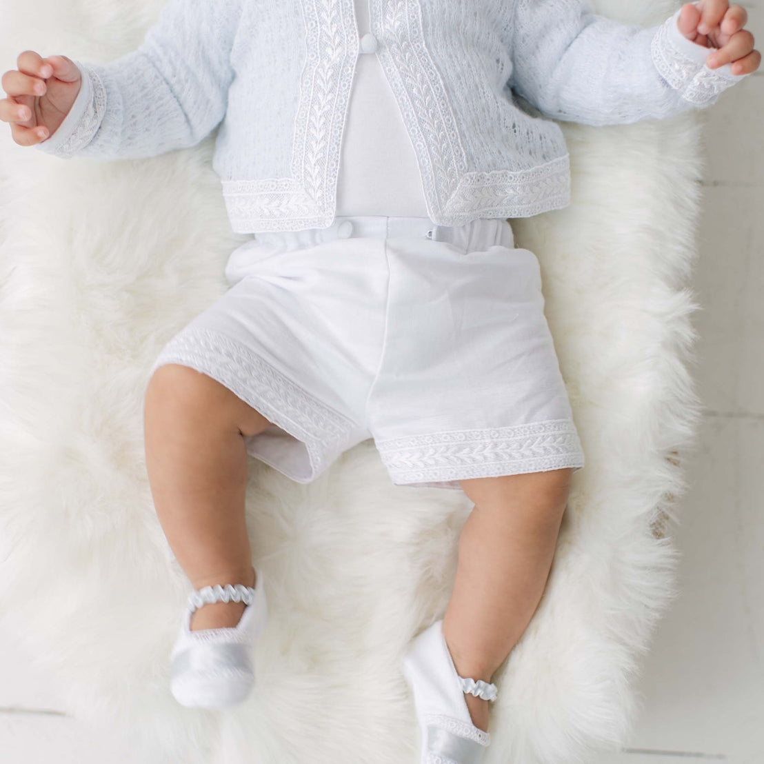 Baby in white outfit with blue knit sweater and lace details on a white fluffy surface