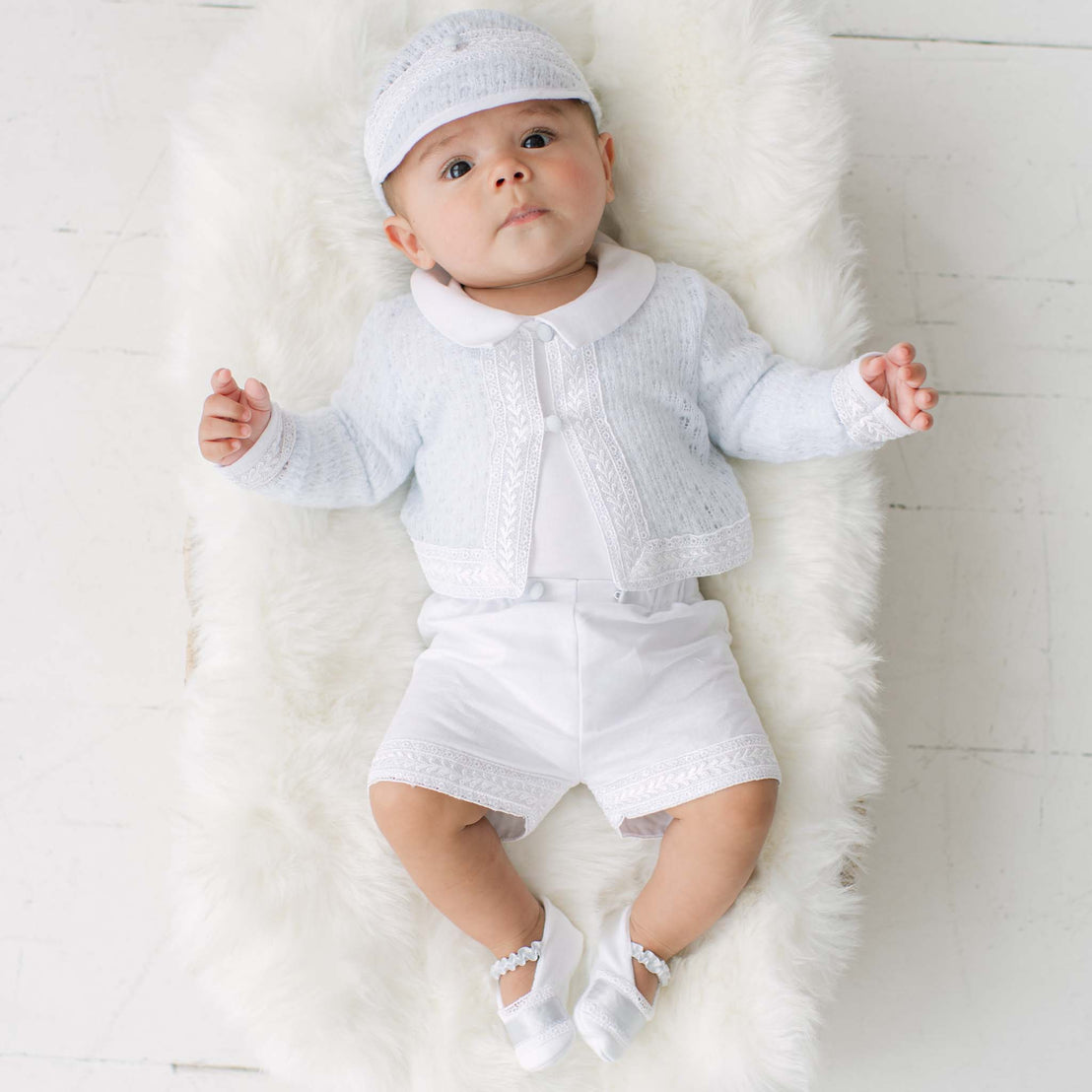 Baby in a blue knit sweater and matching white shorts lying on a white fur rug.