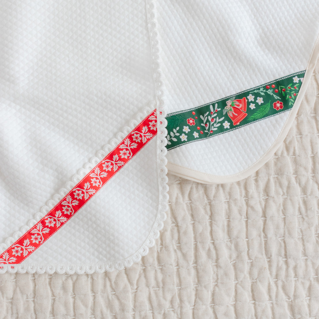 Close-up of two white quilt blankets with a red and green ribbon.