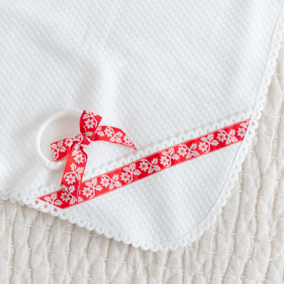 Red and white ribbon headband on a matching white quilted blanket with edge lace detail.