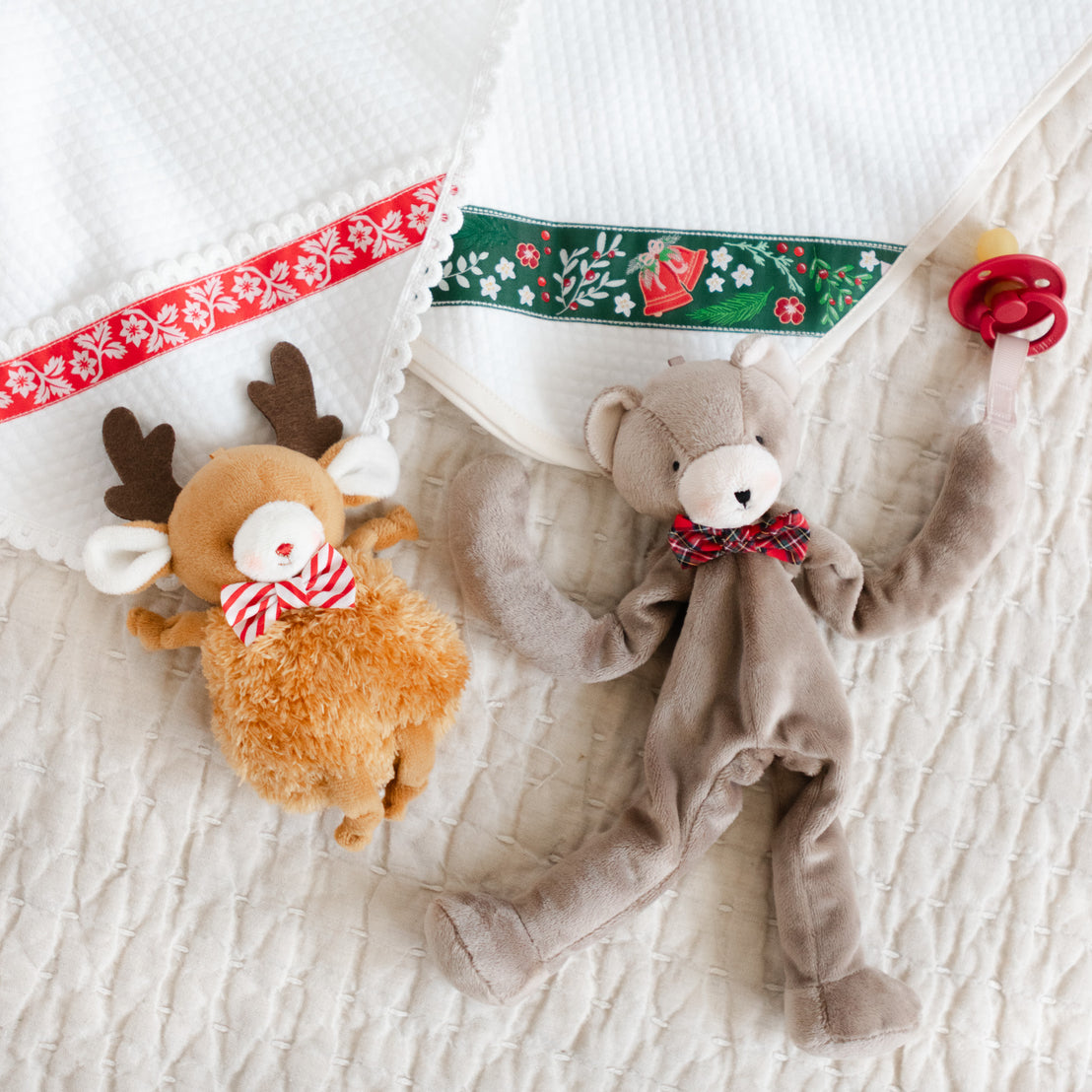 Two plush toys, a reindeer and a bear, near two white quilt blankets.