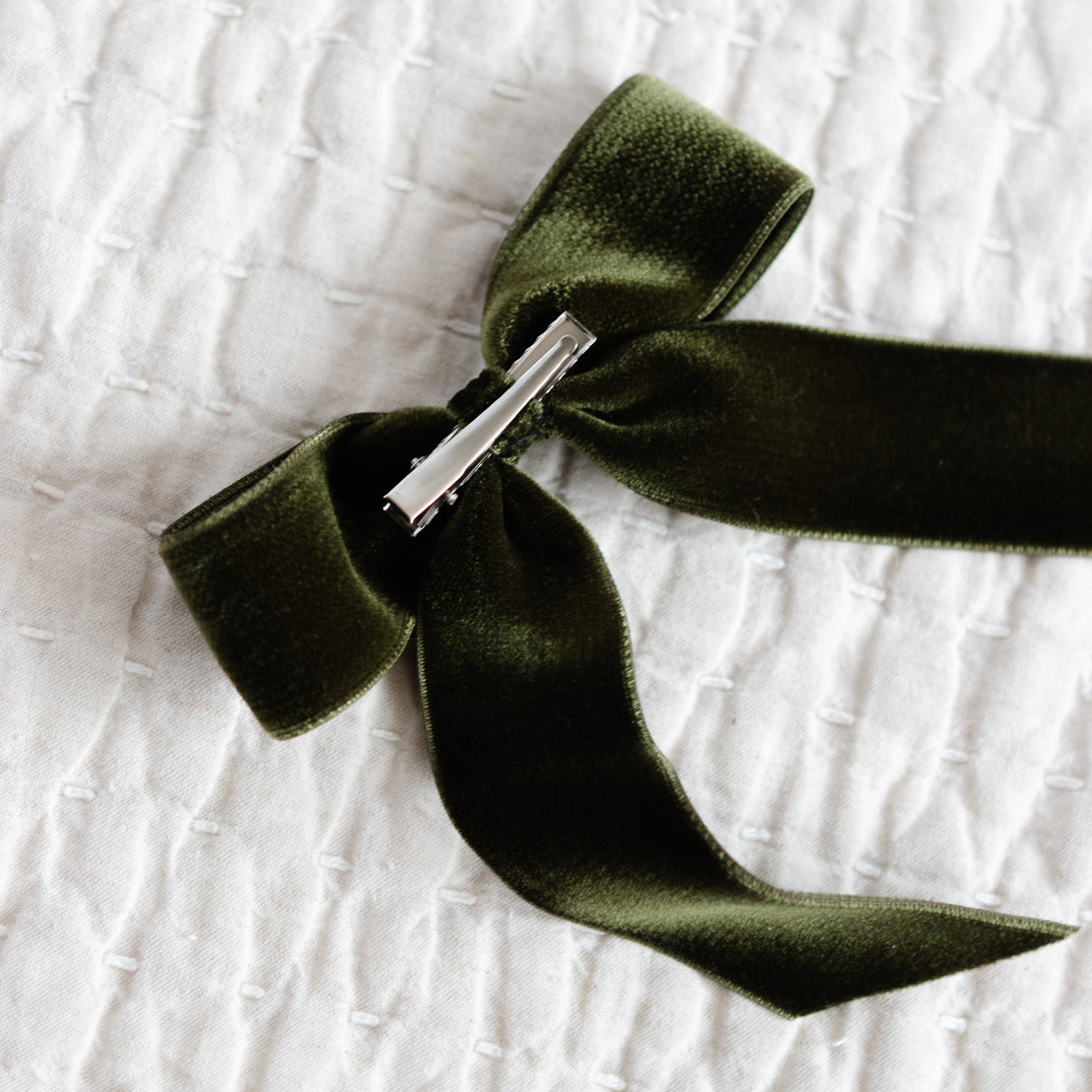 Green velvet ribbon with a silver clasp on a textured white background.