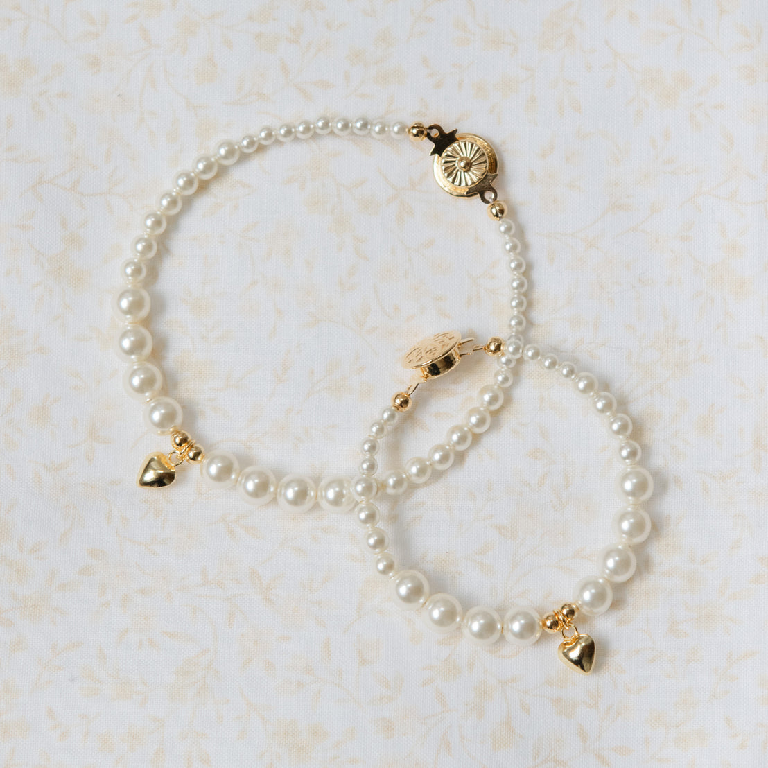 Pearl bracelet with gold charms on a light beige background