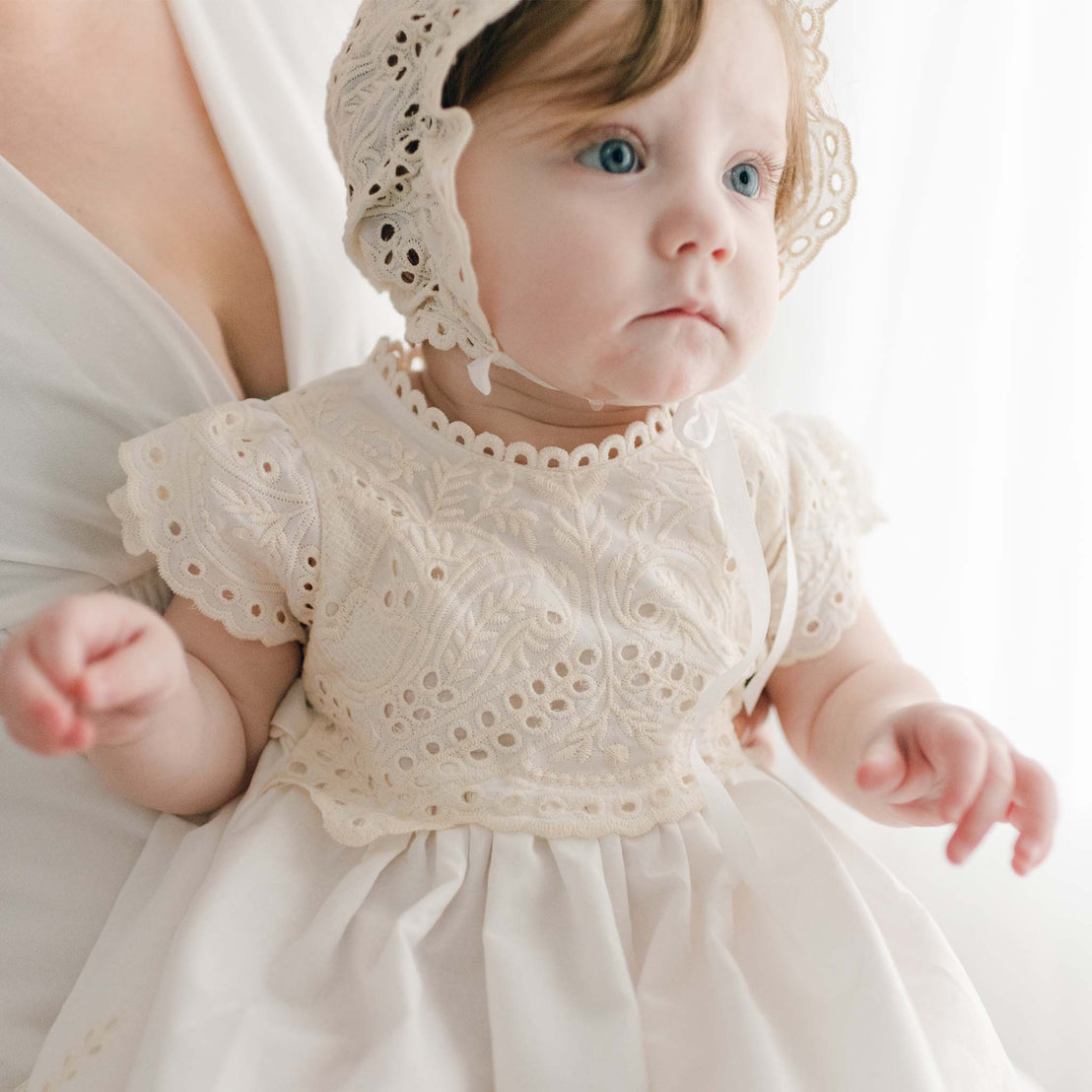 Baby wearing an Ingrid cotton blessing gown in light ivory and a bonnet