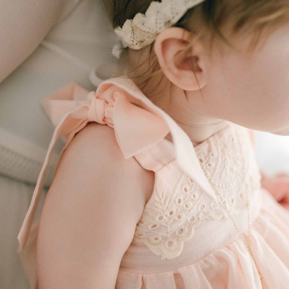 Baby wearing the pink Ingrid Romper Dress. The photo showcases the pink tie straps on her shoulders