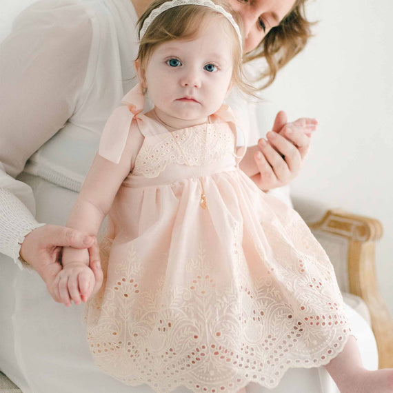 Baby girl sitting on her mother's lap and wearing a pink Ingrid Romper Dress and lace headband
