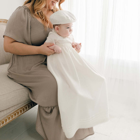 Baby boy wearing the convertible baptism gown and Romper Skirt Set. The skirt attaches to the Oliver Romper to turn the romper into a traditional christening gown. He is also wearing the Oliver Linen newsboy Cap.