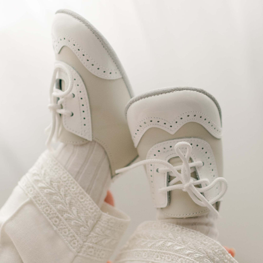 A close-up of elegant Boys Ivory Two Tone Wingtip Shoes with intricate detailing and perforations, against a soft, light background. These vintage boots are truly an upscale heirloom piece.