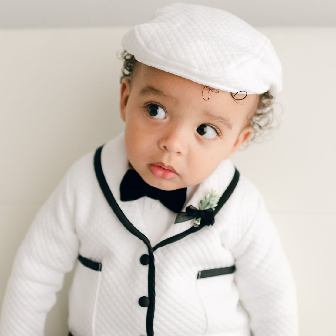 Baby boy wearing the white James 3-Piece Suit, including the jacket, pants, and onesie (with matching Newsboy Cap).