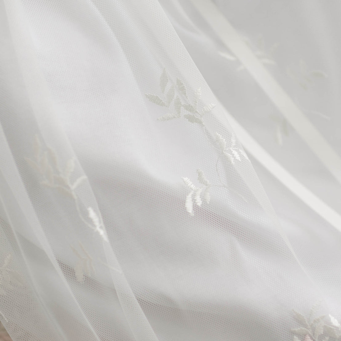 Delicate, sheer Joli Christening Gown with embroidered netting, gently diffusing sunlight, creating a soft and tranquil ambiance.
