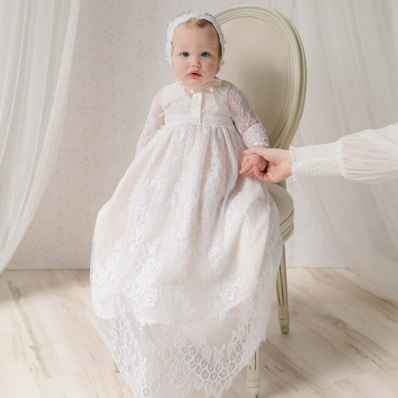 Baby in a white lace dress sitting on a chair with a neutral chiffon background