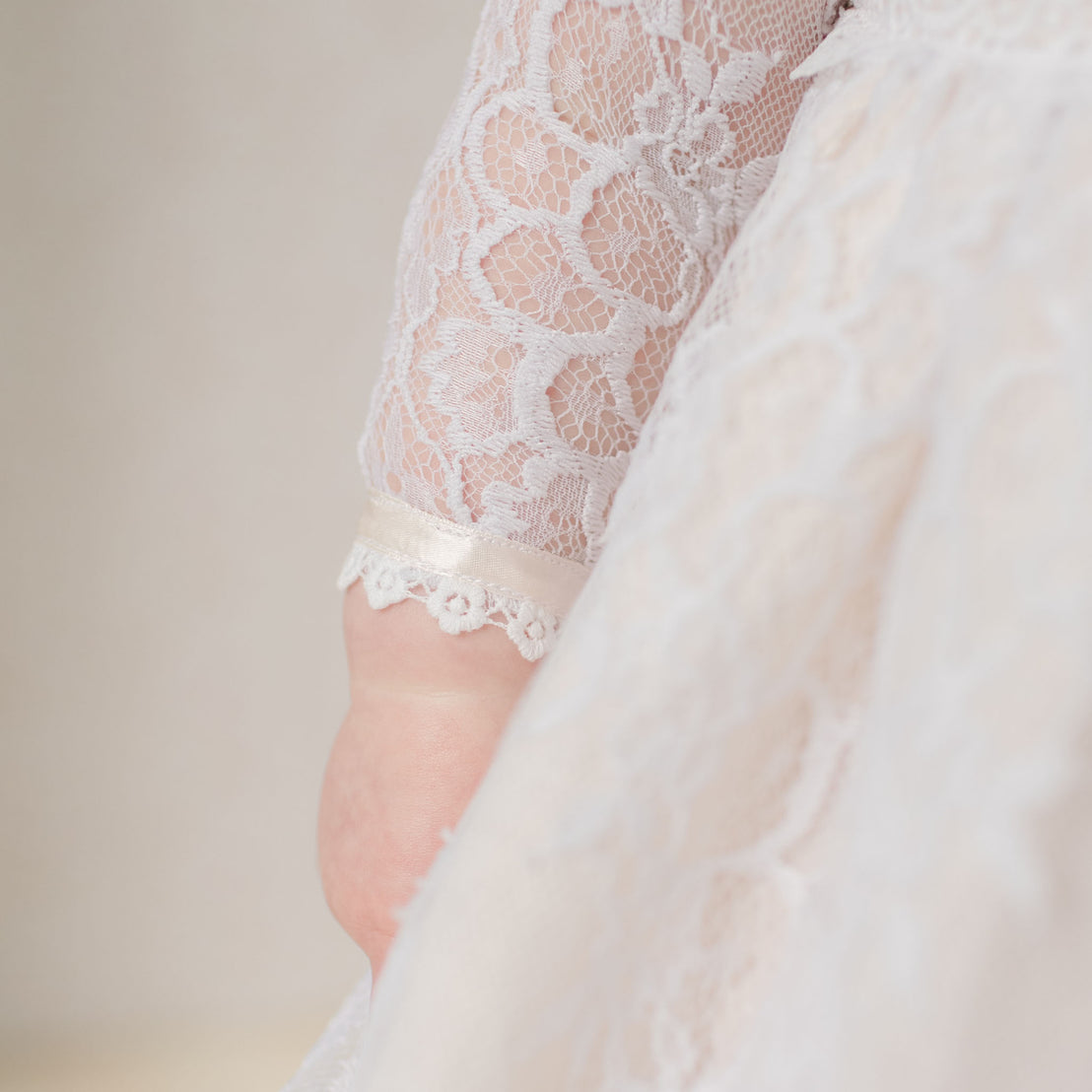 Close-up of a lace-trimmed sleeve on a white garment against a neutral background