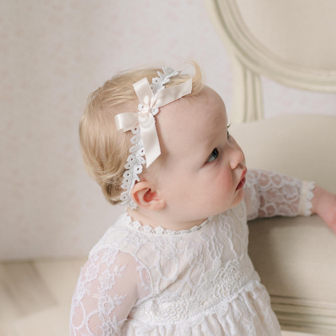 Baby wearing a white lace dress and headband with a pink bow.