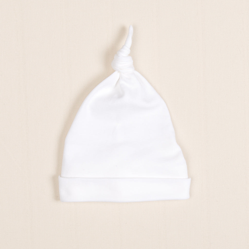 Flat lay photo of the Newborn Knot Cap made with soft pima cotton in white and featuring a knot design