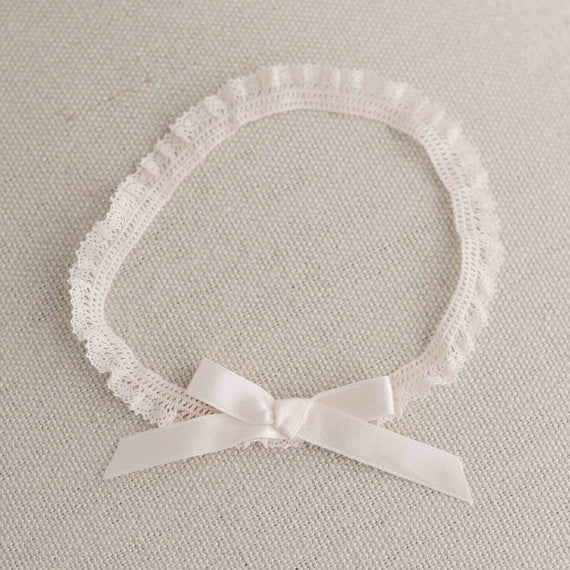 A delicate Ava Headband with a small blush pink silk ribbon, displayed flat against a soft beige textile background.