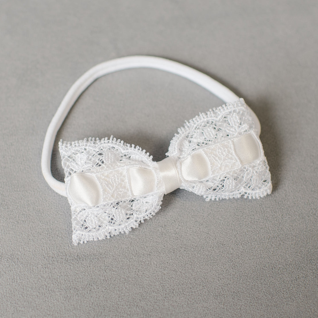 Aria Lace Bow Headband on a grey background, featuring intricate Aria lace details and a silk center.