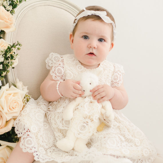 Baby girl holding plush lamb doll in her fancy baby dress.