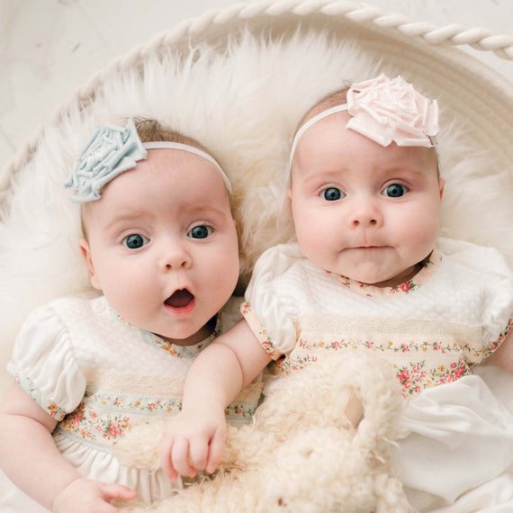 Two twin baby girls wearing two different color variations of the Eloise Linen Flower Headband. The headband features a flat linen rose in light blue or light pink.