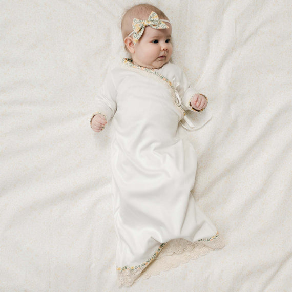 Newborn baby in the Lillian Layette
and matching Headband Bow laying on a floral patterned blanket. Part of Baby Beau & Belle's Coming Home Outfit Collection.