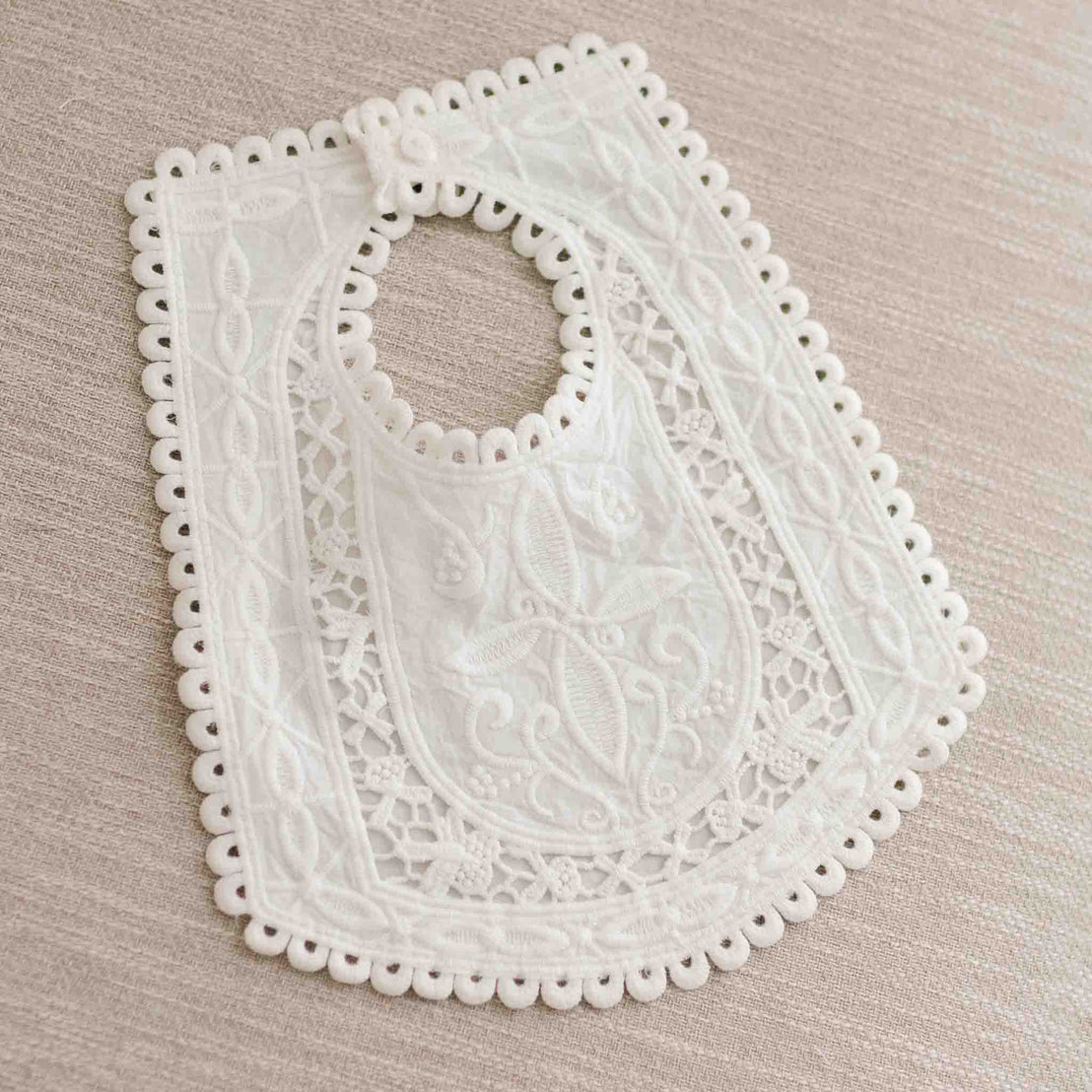 Flat lay photo of the Lily Lace Bib that is made out of cotton lace in light ivory and exhibits a unique squared design and circle lace trim