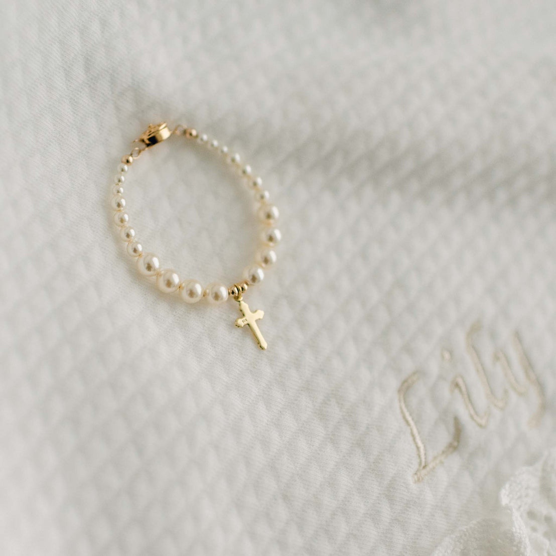 Gold cross pearl bead bracelet on blanket