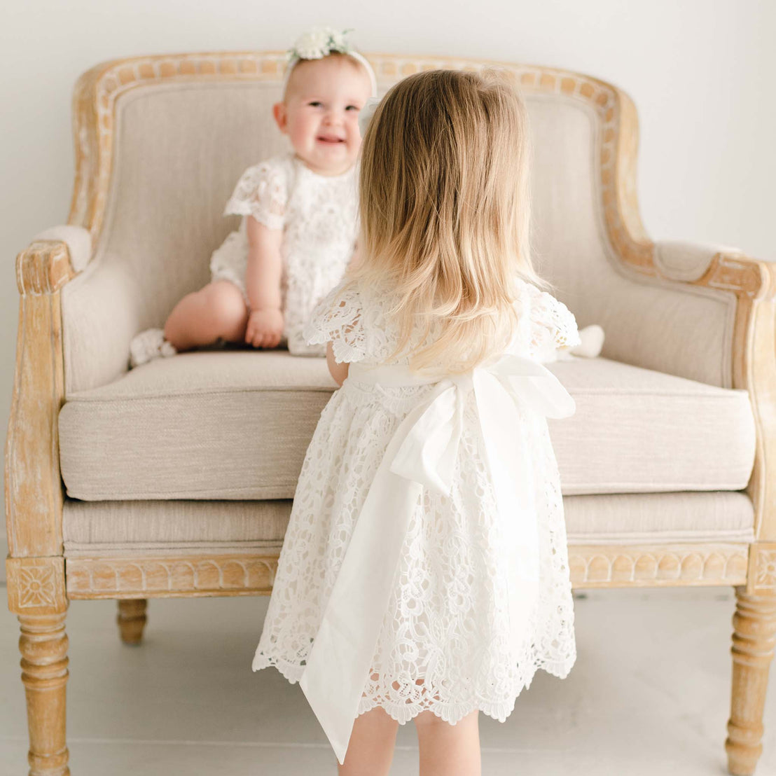 Two baby girls wearing the Lola Dress. Detail shows the back of the dress with ties in back and sash.