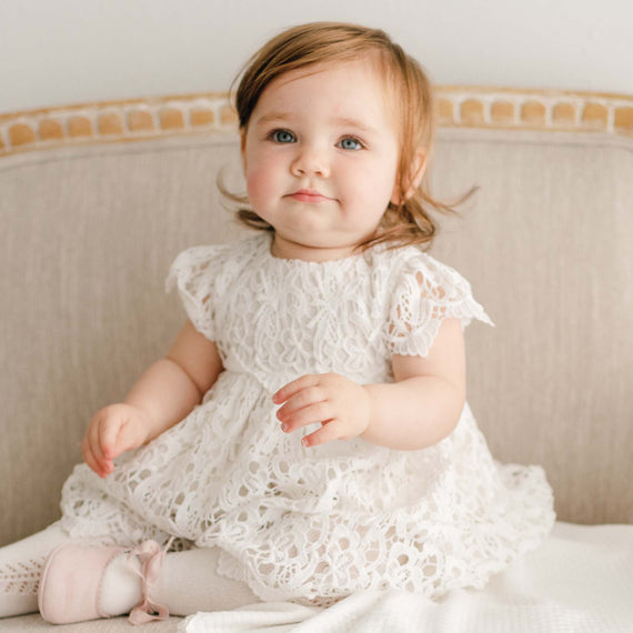 Baby girl wearing the Lola Dress. Dress is made with cotton lining in light ivory featuring an all-over lace overlay.