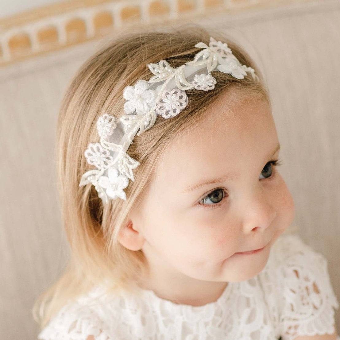 Toddler girl wearing the Lola Beaded Flower Headband, featuring a velvet elastic band with pastel pink and ivory floral appliqué, looking to the side with puckered lips.