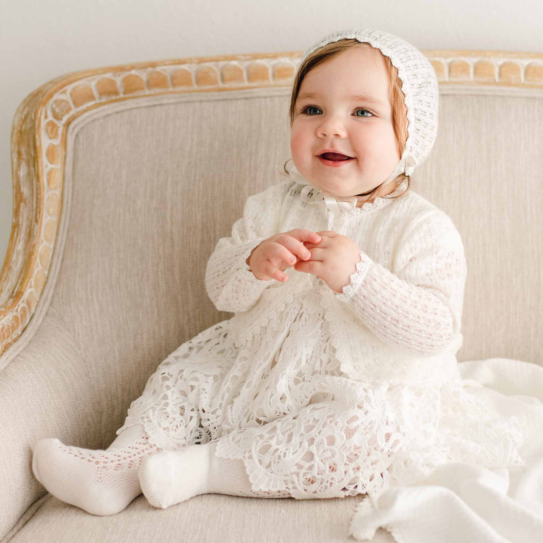 Baby girl wearing the Lola Knit Sweater and Bonnet that matches the Lola Christening Gown, Dress and Romper. Made of 100% ivory knit acrylic in light ivory, a soft and breathable knit.