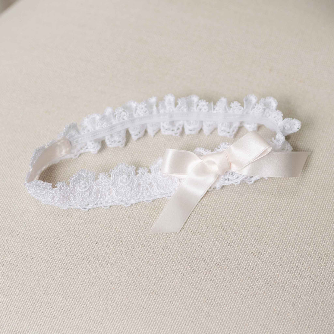 Flat lay photo of the Melissa Lace Headband set against a beige linen background. Details show a white Venice lace with a light pink silk ribbon bow. Perfect for baptism gifts from godparents. 
