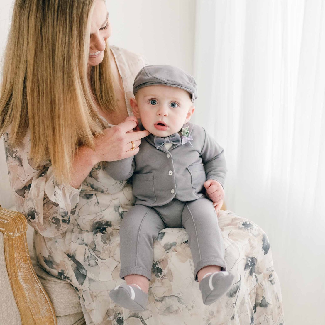 Baby boy in grey cotton suit holding mom's finger in lap