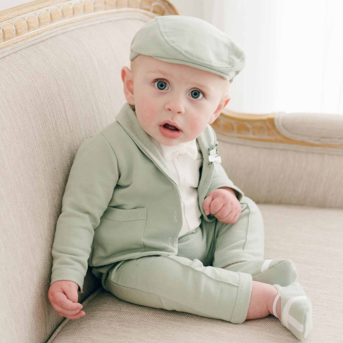 Baby boy sitting in sage green suit, newsboy cap and booties
