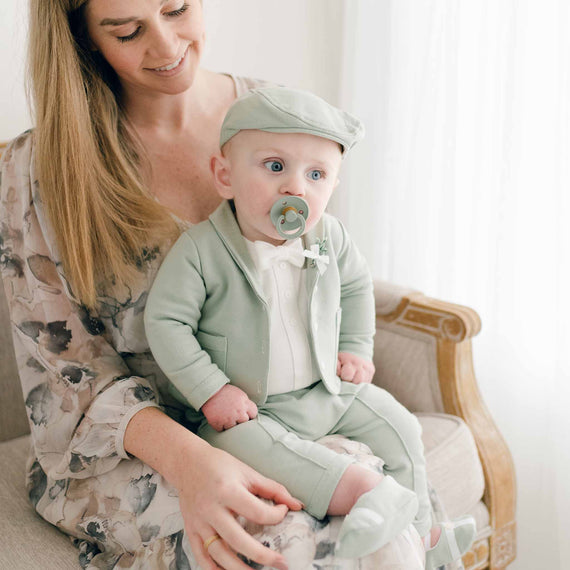 Baby boy sitting in mom's lap in sage green cotton suit and newsboy cap
