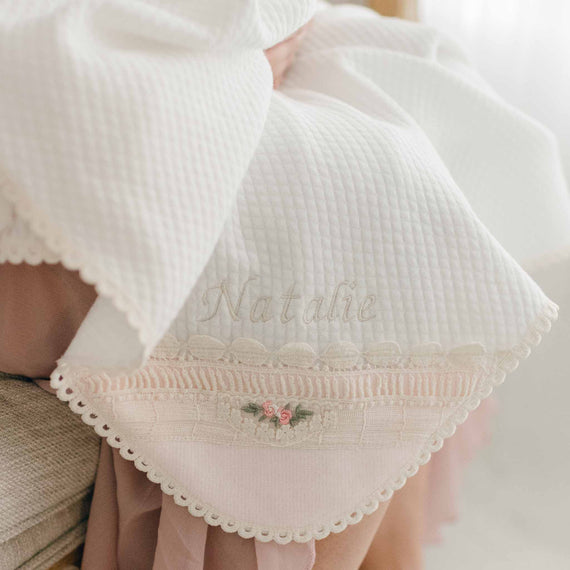Photo of the Natalie Personalized Blanket made from an ivory cotton with a vintage natural cotton lace featuring embroidered pink rosettes, olive green leaf and pink ribbed cotton on one corner. The name "Natalie" is embroidered on the corner of the blanket