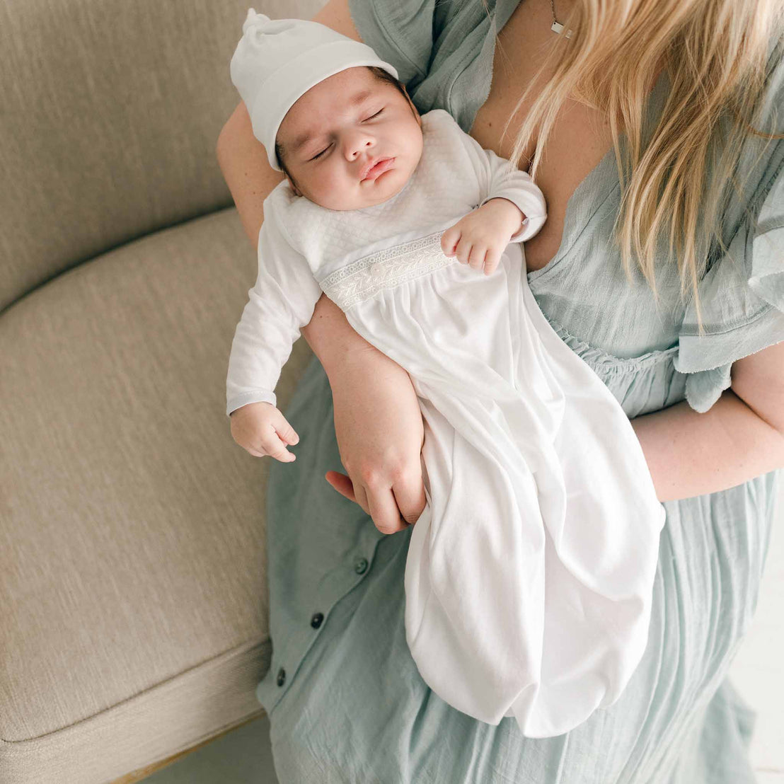 A mother cradling her newborn baby dressed in the Harrison quilted gown, showing the outfit's cozy texture and elegant lace detail.