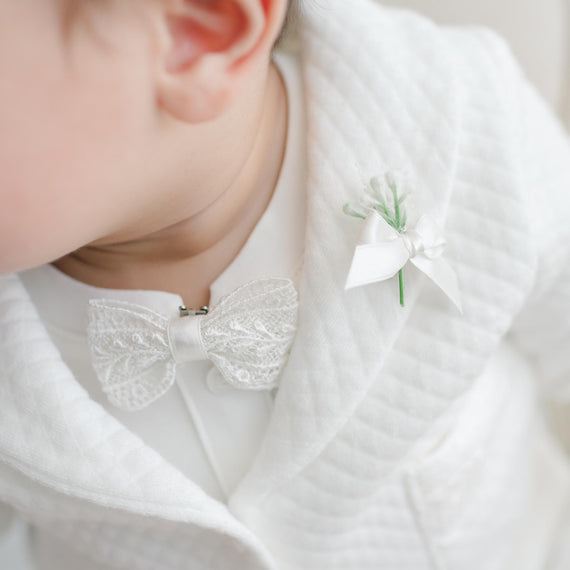 Close-up of a baby wearing a white lace bow tie and boutonniere.
