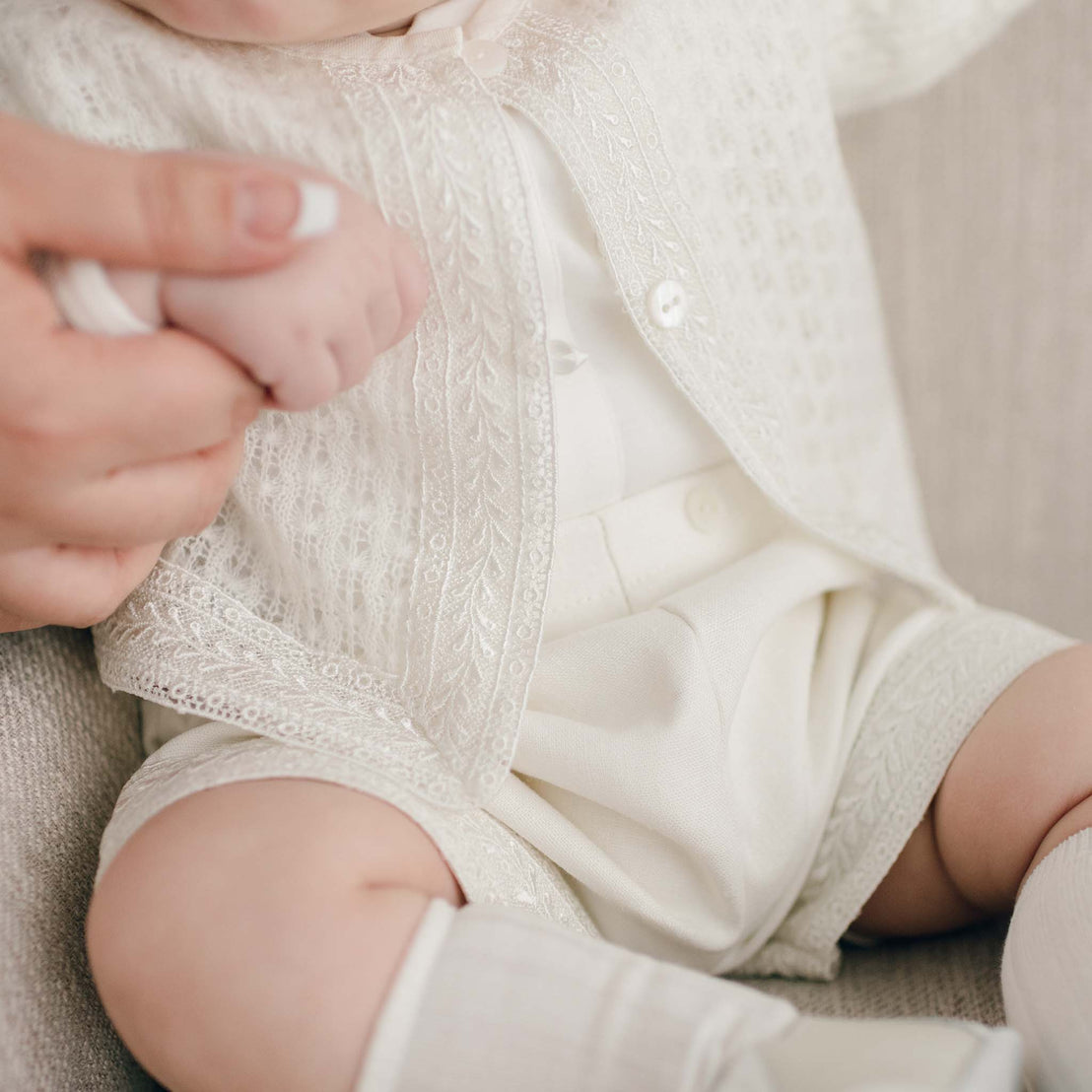 A close-up photo of a baby dressed in the light ivory Oliver Sweater Shorts Suit Set, showing the intricate details on the sweater's knit fabric.