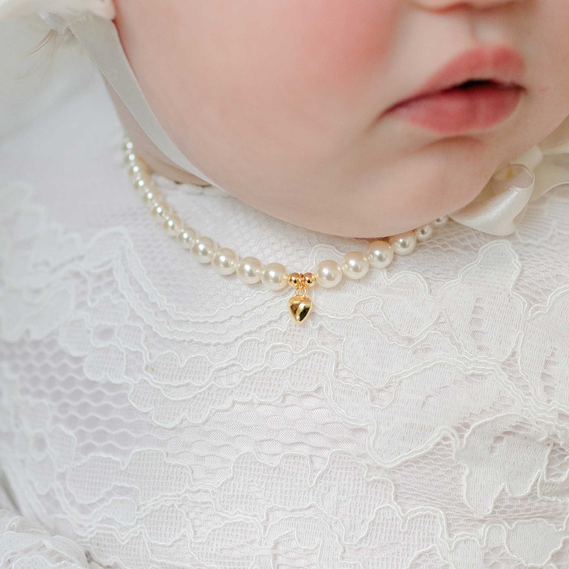 Close-up of a baby wearing a pearl necklace with a gold heart charm.