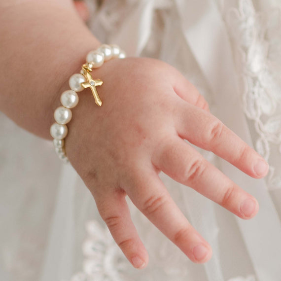 Close detail of Cream Luster Pearl Bracelet with Gold Cross on a baby girl's wrist.