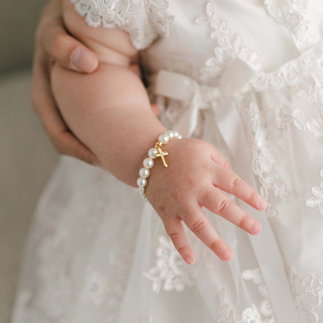 Baby girl wearing the Cream Luster Pearl Bracelet with Gold Cross. Made with cream color Swarvoski pearls, gold plated beads and gold plated clasp.