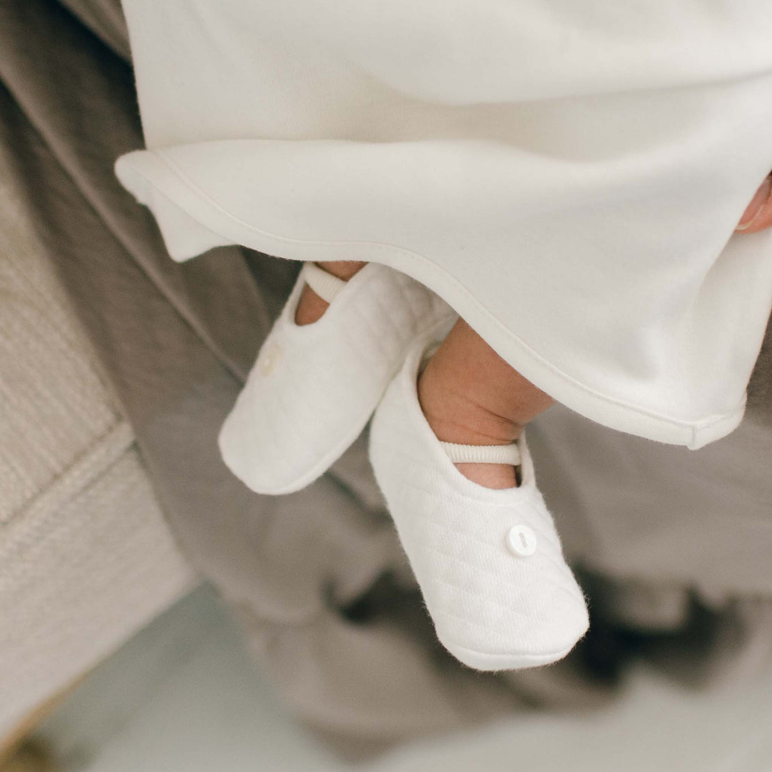 Baby girl wearing the Ivory Quinn Booties made with quilted textured cotton, lined in a matching pima cotton, with a soft stretch strap, and button detail on the front.