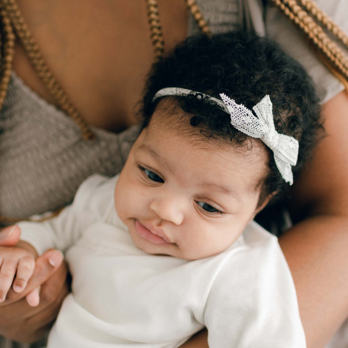 Baby girl wearing the Quinn Lace Headband that complements her Quinn Layette Gown.