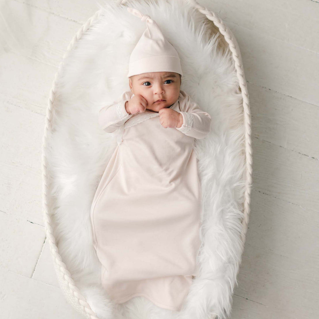 Baby girl in pink newborn layette gown and cotton knot hat laying in basket