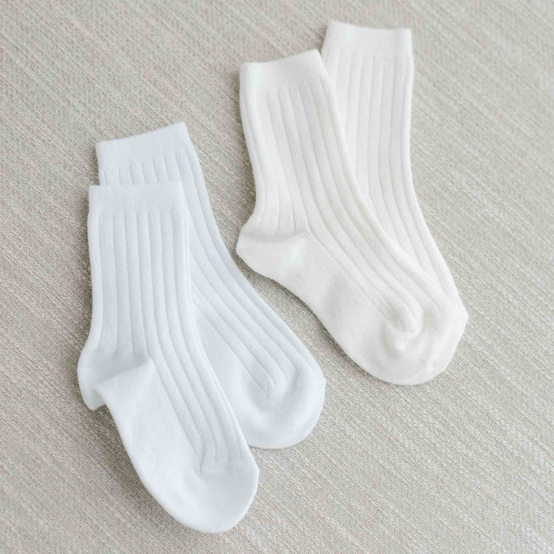 Flat lay photo of two pairs of socks, including both the white and cream Ribbed Knee Socks. These socks are made from a cotton blend and feature a ribbed pattern