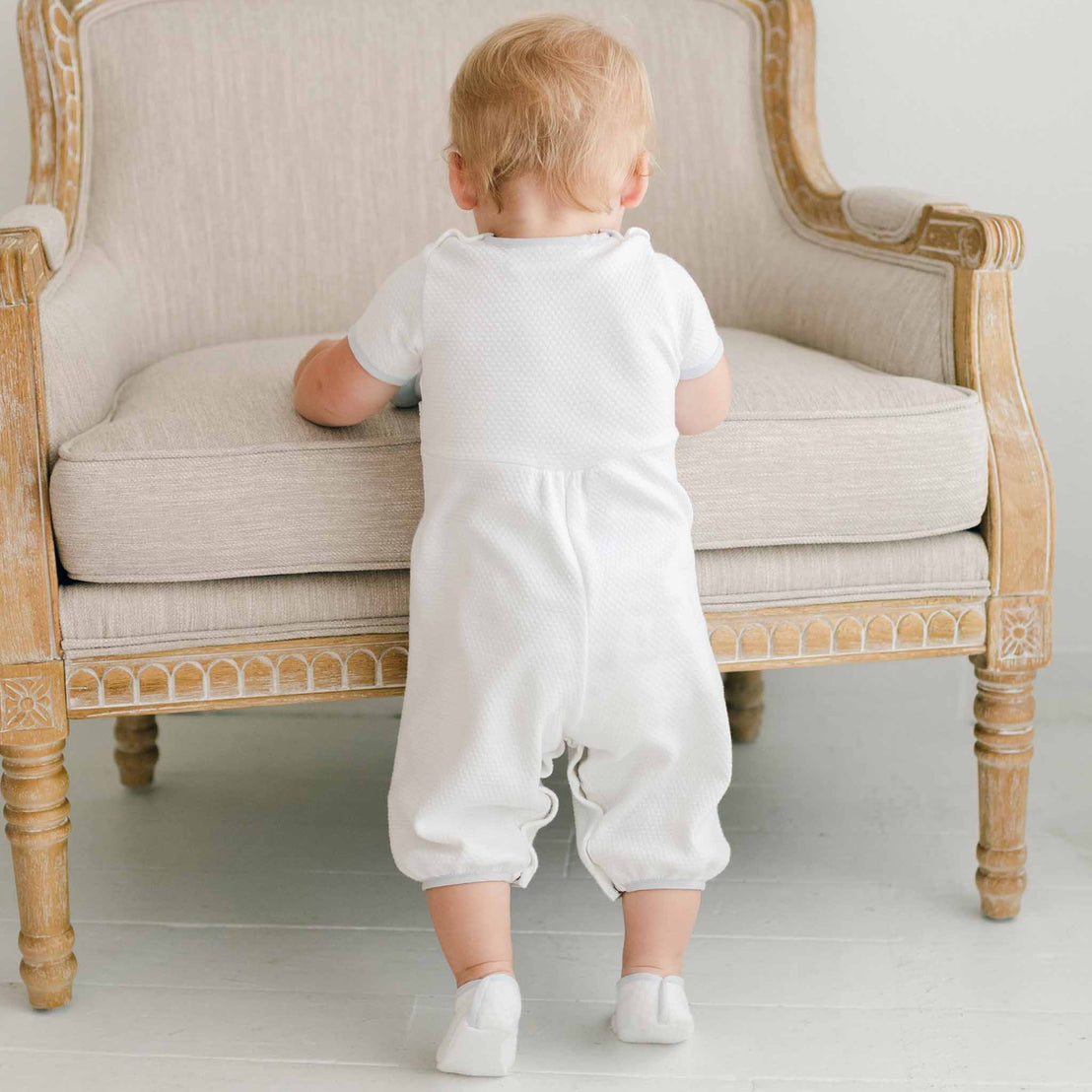 Back detail of baby boy wearing the Harrison Short Sleeve Romper, featuring the hidden snaps at the legs and buttons at shoulders