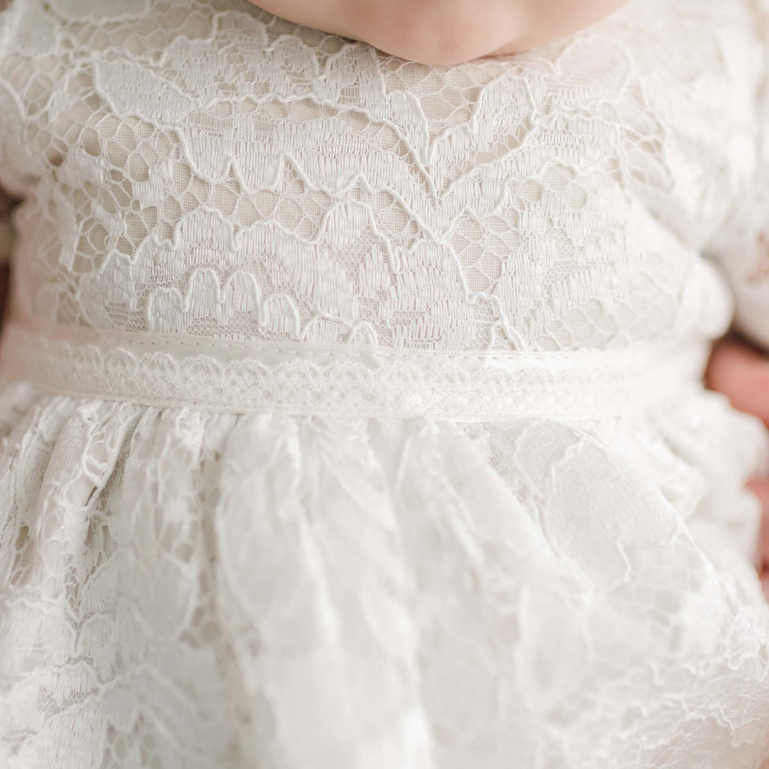 Close-up of a baby wearing a Rose Romper Dress, focusing on the detailed fabric and design around the waistline and bodice.