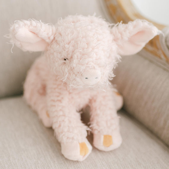 A soft, plush Hammie Pig with curly pink fur and floppy ears sitting on an upscale beige couch, giving a cozy and adorable appearance.