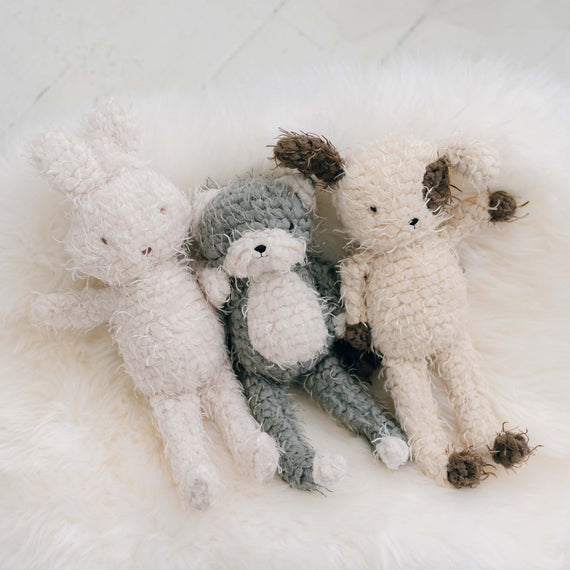 Four shaggy pals in different shades of white and gray are arranged in a cuddly group on a soft, white furry surface, perfect as a baby shower gift.